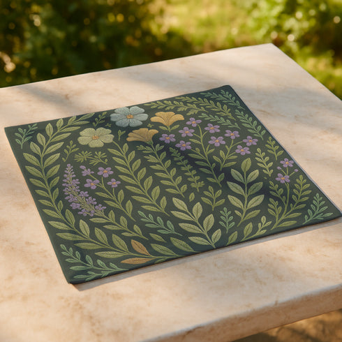 A 4-piece cloth napkin set featuring embroidered-style botanical illustrations of wildflowers and herbs in shades of gold, mint, and lavender on a dark green background; made from soft polyester, square-shaped, with a luxe and mystical design.